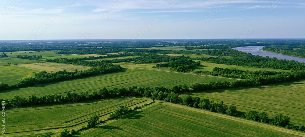 Fototapeta premium Aerial view of lush farmland landscape with winding river under blue