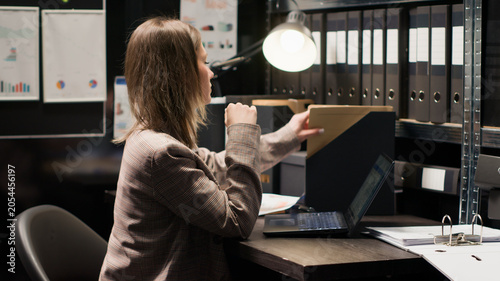 Foto Caucasian policewoman inspecting evidence, reviewing records, and utilizing technology in a well-organized office space, Dedicated investigator analyzes witness statements and records to solve crime