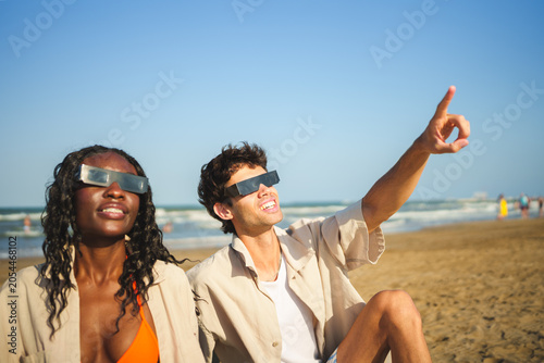 Cuadro en lienzo Two people on beach wearing solar eclipse glasses, man pointing to sky