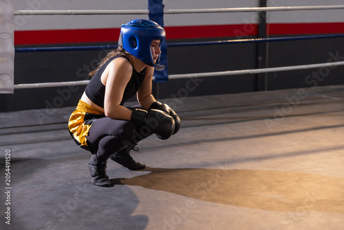 Blue protective headguard and black gloves are resting on boxing ring floor near ropes
