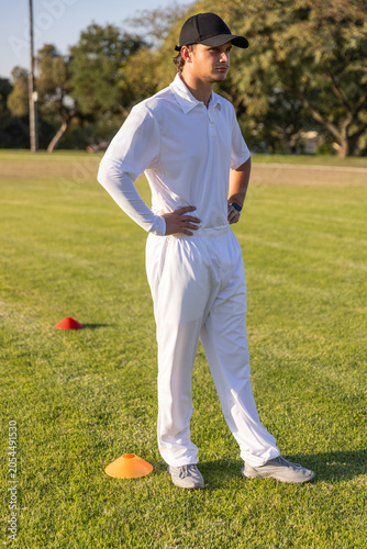 Cricket player is standing with hands on hips on grassy field near orange and red cones