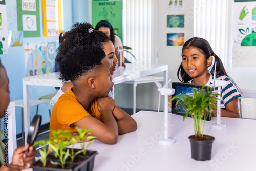 Diverse teacher and elementary students exploring plants, using wind models and tablet at table