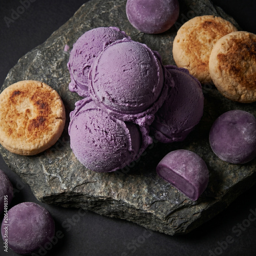 Ube ice cream scoops displayed on a dark stone with artisanal cookies