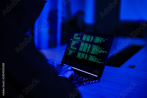 Tableau sur toile Mysterious hacker in black hoodie stealing confidential data on laptop