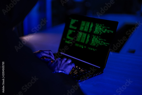Photos Mysterious hacker in black hoodie stealing confidential data on laptop