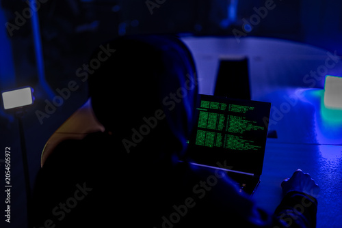 фотографія Mysterious hacker in black hoodie stealing confidential data on laptop