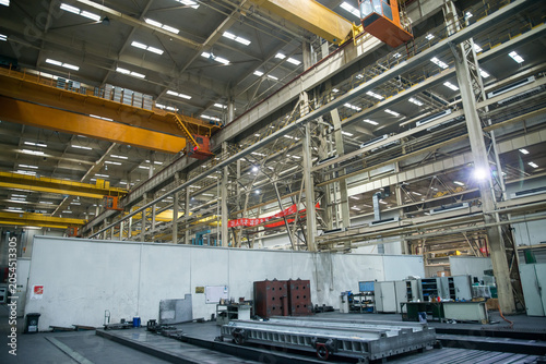 Large industrial factory workshop interior with overhead cranes and heavy machinery
