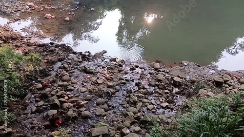 High angle view of rocky riverbank with sky and sun reflections shimmering on the water surface