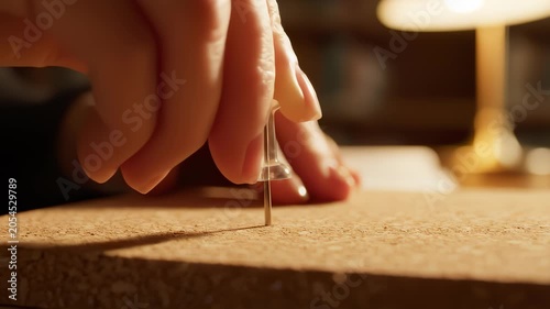 Hand Pressing A Clear Thumbtack Into A Brown Cork Board Surface