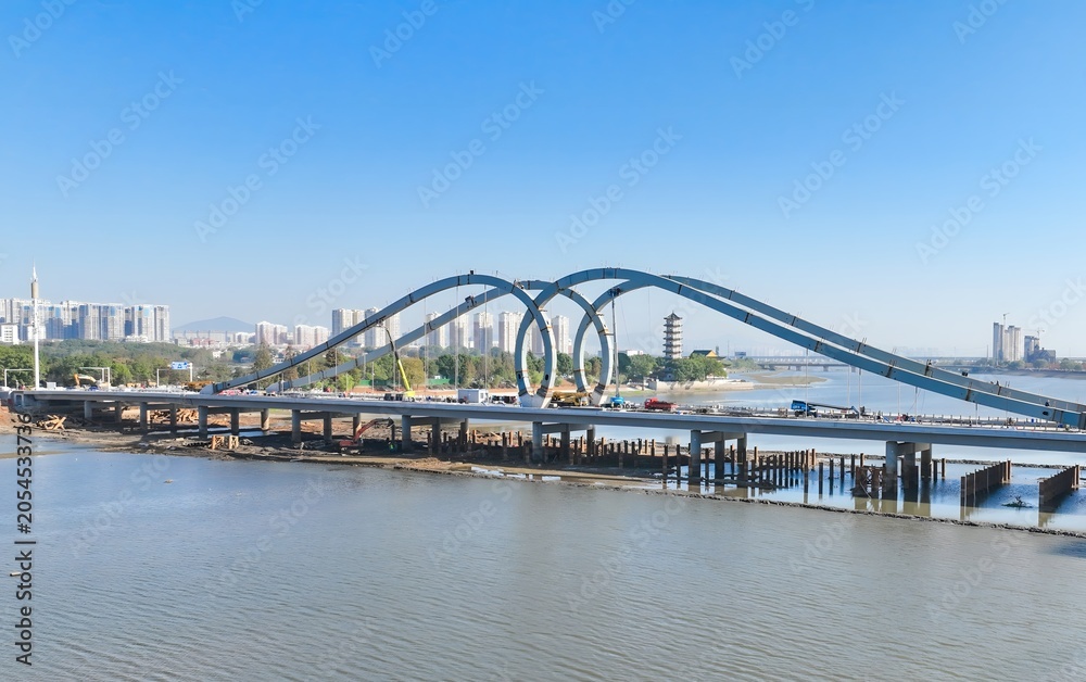 Naklejka premium Modern Blue Loop Bridge Over River with City Skyline