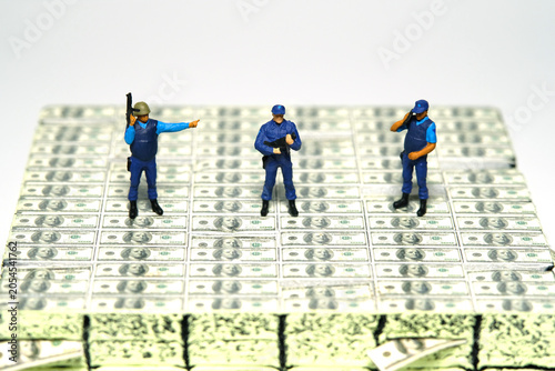 Miniature people toy figure photography. Money transfer security concept. A police officer standing above money cargo pallet. Isolated on grey background