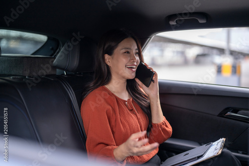 Woman working and talking on smartphone in car backseat