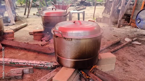 Large aluminum steaming pots placed over an outdoor open fire stove using rustic wood logs to cook traditional food like rice cakes.