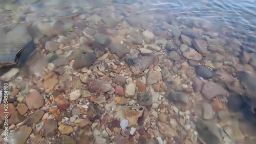 A perspective view of small colorful pebbles lining the seabed under transparent, gently rippling sea water.