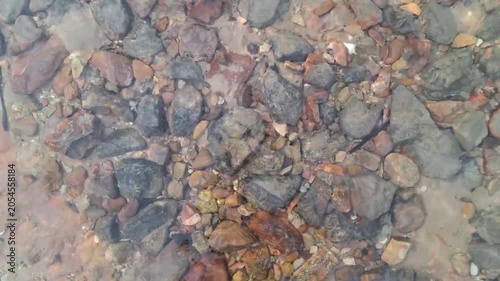 Top view of jagged and textured dark gray and brown stones submersed under clean, clear rippling water.
