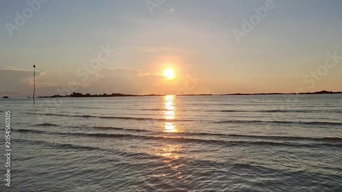 A beautiful sunset view over a calm ocean during low tide, with the sun reflecting a brilliant golden light onto the water surface.