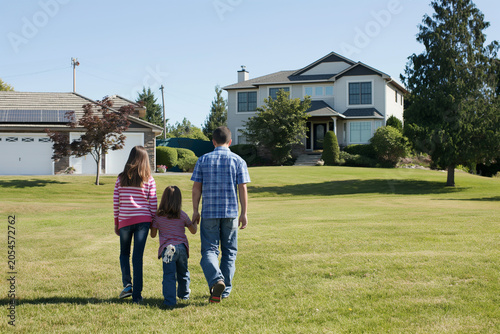 A man and two children walk through a grassy yard