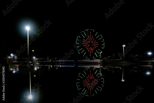 Фотография A brightly lit Ferris wheel stands out against the dark sky, casting colorful reflections
