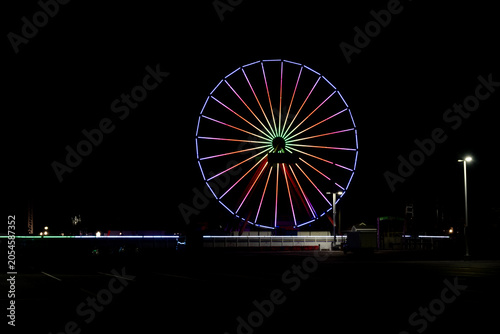 Фотография A Ferris wheel brightly lit with colorful lights is set against the dark night sky
