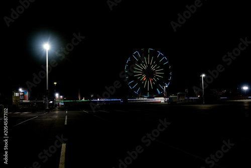 Bild auf Leinwand A brightly lit Ferris wheel stands out against the dark sky, casting colorful reflections