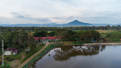 Aerial view of rural village with rice fields, river, and misty volcanic mountain in the background, West Sumatra, Indonesia