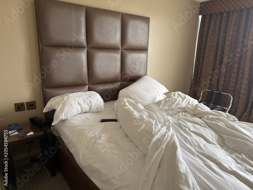 Valokuva Unmade Hotel Bed with Large Brown Padded Headboard and White Linens