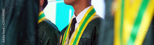 Bild auf Leinwand Close-up of a student wearing a green graduation gown with a yellow and green sash during a commencement ceremony, representing education, achievement, and academic success