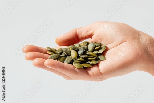 A person holds a handful of green pumpkin seeds against a white background