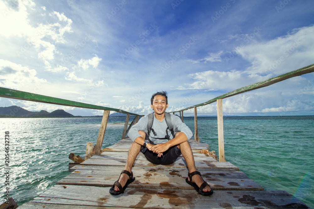 Naklejka premium Happy Traveler Sitting on Wooden Pier Above Tropical Sea