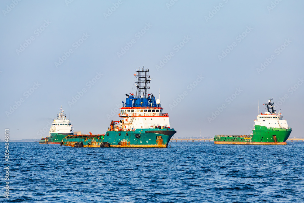 Fototapeta premium Offshore supply vessels and anchor handling tug ships anchored at open sea water near maritime port area