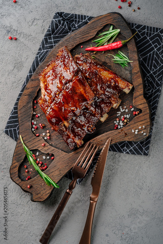 Sticky glazed pork ribs with barbecue sauce, garnished with fresh rosemary and red chili pepper on rustic wooden board. Juicy grilled spare ribs, delicious meat dish, gourmet barbecue style, top view