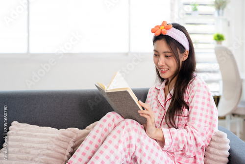 Young woman in pyjamas writing on notebook sitting on sofa at home.