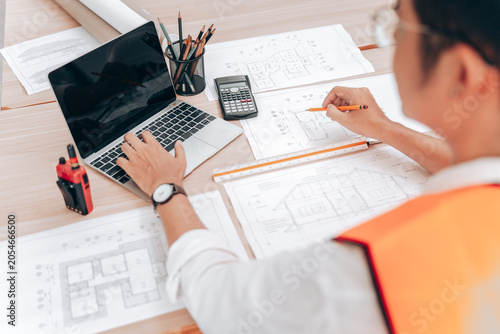 Architect Working on Building Plans at Desk with Laptop and Tools