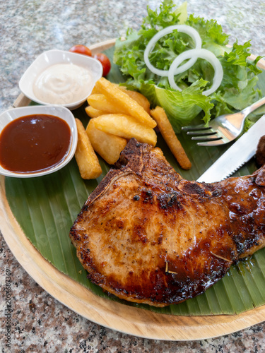 Grilled Pork Chop Steak on Banana Leaf Wooden Plate with French Fries Fresh Salad and Sauces