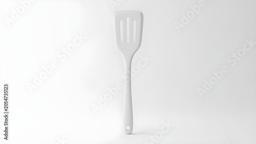 A shiny metal spatula stands alone on a clean white surface indoors.