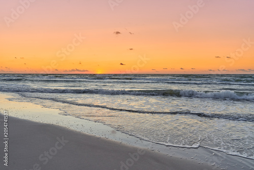 Golden summer sunset over the Baltic Sea with soft waves and sandy shoreline. Tranquil evening seascape with colorful sky and peaceful coastal atmosphere.