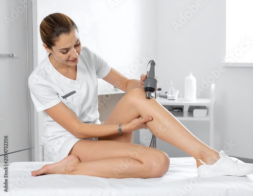 Focused Female Physiotherapist Applying Therapy Device to Bare Leg in Clean Medical Clinic