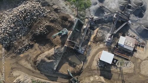 Aerial View of Excavator Processing Ore Near Rock Crusher Facility in Mining Quarry, Construction and mining site view from above.