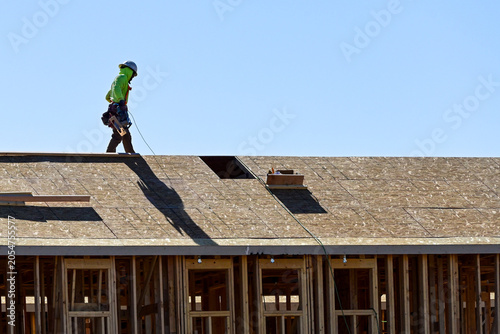 Carpenter using fall protection gear while working on the roof of a two story single-family home under construction, representing residential framing, elevated work, and housing development activity