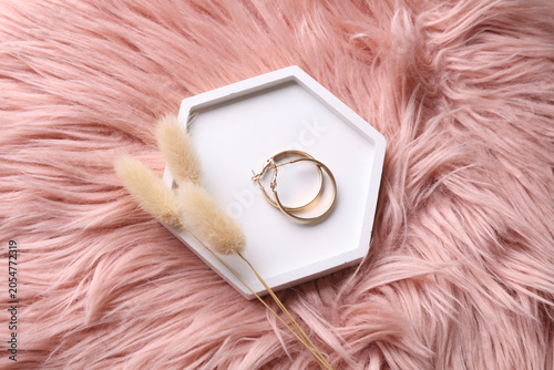 Gold earrings in a plaster tray with dry grass on a pink fleecy background