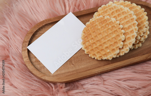 Delicious waffle discs in tray with white business card on pink background