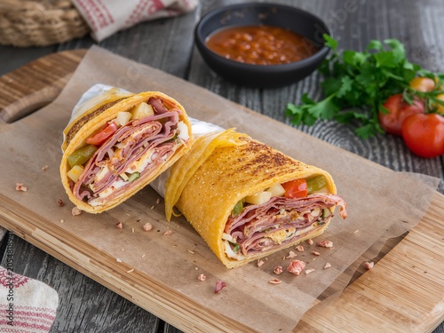 Salami meat wrap with vegetables and sauce on board