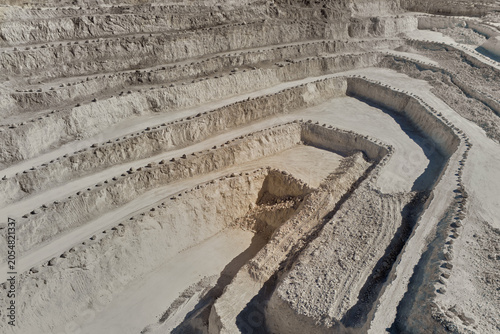 Drone view of a large terraced limestone quarry with winding haul roads and stepped excavation levels. Industrial mining landscape showing mineral extraction, raw materials production and quarry engin