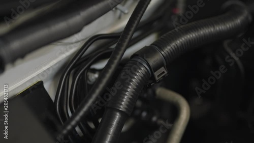 Close-up of black corrugated automotive wiring hose and thin metal brake lines under the hood of a car.