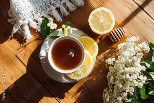 Top-down view of a wooden table with tea, honey, and wildflowers, one bee landing on a lemon slice, bright and airy breakfast aesthetic