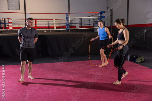 Photos Male coach with whistle timer watching two women trainees skipping ropes barefoo