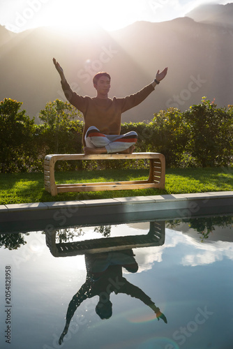 Wooden bench is resting on manicured lawn by pool, sunlight is creating lens flare and reflection