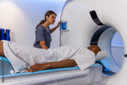 African American tech in scrubs operating touchscreen while preparing male patient on CT table