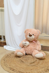 Decoration as a background for photos with the newlyweds. A white curtain, bouquets of roses, a teddy bear holding a heart with the words "I love you" and a gift box with best wishes written on it