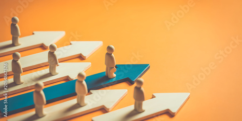 A group of people standing on arrows pointing in different directions on an orange background, symbolizing individuality and diverse paths in business or life